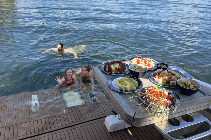 Gäster badar bakom båten bredvid ett bord med frukt och tilltugg